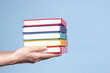 © vejaa - Female hands holding pile of books over light blue background. Education, self-learning, book swap, hobby, relax time