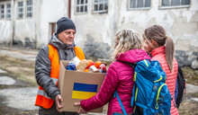Volunteer In Orange West Gives A Box Of Food Donation To Fleeing Refugees From Ukraine