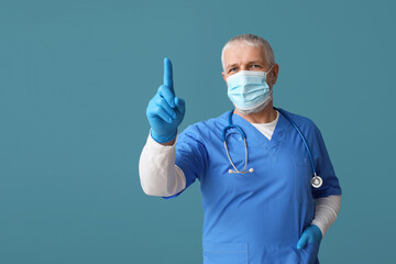 Wall Mural - Mature male doctor in medical mask with raised index finger on blue background