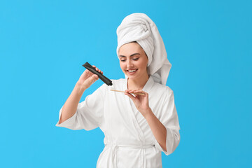 Wall Mural - Beautiful young woman in bathrobe, with activated charcoal tooth paste and brush on blue background