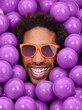 © Alexandra W/peopleimages.com - Looking cool and crazy. A young black mans face amongst purple pit balls.