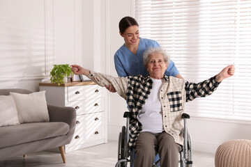 Wall Mural - Senior woman in wheelchair doing physical exercise and young caregiver helping her indoors. Home health care service