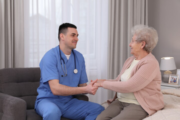 Young caregiver talking to senior woman in bedroom. Home health care service