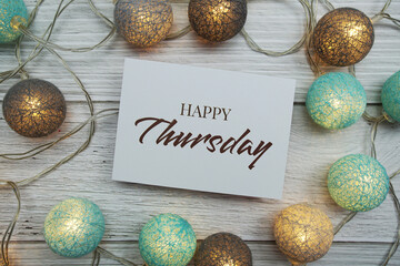 Wall Mural - happy thursday text on paper card with led cotton balls top view on wooden background