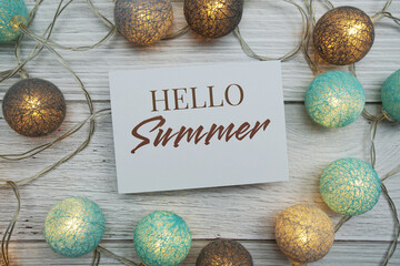 Wall Mural - hello summer text on paper card with led cotton balls top view on wooden background