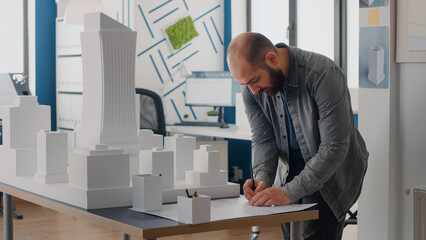 Poster - Man engineer analyzing building model to design blueprints plans on table. Architect working with maquette to plan construction layout and urban property development. Architecture project
