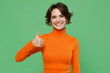 © ViDi Studio - Young smiling happy satisfied fun positive woman 20s in orange turtleneck showing thumb up like gesture isolated on plain pastel light green color background studio portrait. People lifestyle concept.