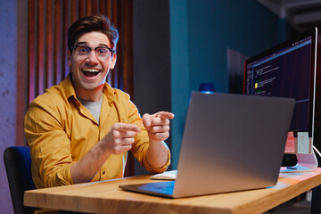 Young surprised happy winner amazed successful software engineer IT specialist programmer man in shirt work at home office writing code point finger on laptop pc computer. Program development concept.