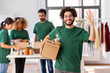 © Syda Productions - charity, donation and volunteering concept - happy smiling male volunteer with food in box waving hand over and international group of people at distribution or refugee assistance center