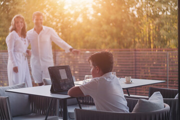 Wall Mural - Happy elderly couple resting on the balcony of a luxury house while their son using a tablet. Selective focus