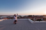 Fototapeta  - Happy family taking a selfie with a smartphone on the roof of their house at sunset. Selective focus 