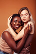 © iordani - young pretty african and caucasian women posing cheerful together on brown background, lifestyle diverse nationality people concept