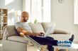 © Studio Romantic - Unhealthy businessman with injured leg in bandage sit on sofa at home work online on computer. Unwell male employee with foot trauma wearing special splint use laptop. Injury and rehabilitation.