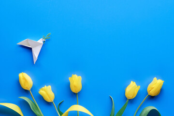 Wall Mural - Dove of peace, paper origami. Peace to Ukraine. Yellow tulips, flowers, on blue background. Copy-space, place for text. Top view, flat lay, concept background.