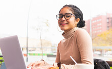 Happy Young Ethnic Woman Taking On Eyeglasses For Working On Laptop