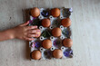 Top shot of a girl's hand touching the tray with eggs prepared for Easter decoration with flower print.