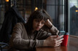 © kanashkin - A girl with curly hair uses a smartphone while sitting in a cafe by the window.