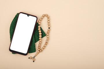 Wall Mural - Top view of smartphone with white screen, next to a rosary on a beige background, mockup