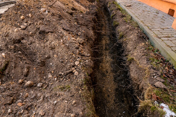 Red and white barrier tape protect a danger place. The warning tape indicates the danger of being on the territory of the construction site. Dug trenches for laying new pipes.