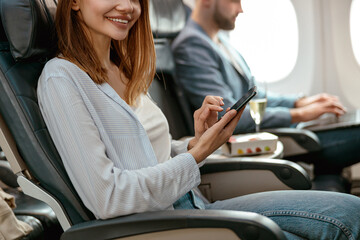 Wall Mural - Cheerful woman using smartphone in passenger airplane