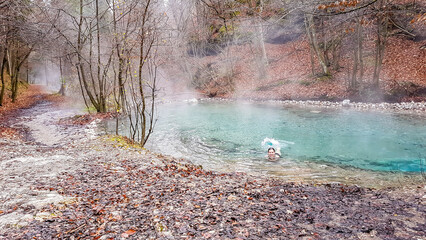 A girl in a black swimsuit swimming in a natural thermic spring in Maibachl, Austria during autumn. The thermic pool is located in the middle of the forest. Healing power of natural water. Relaxation