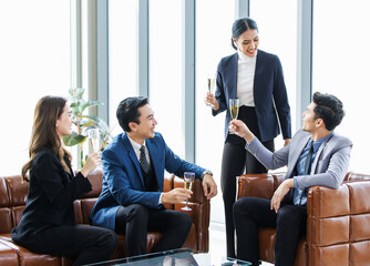 Group of Asian happy cheerful professional successful businessmen and businesswomen in formal suit sitting on leather sofa smiling holding tall champagne glass toasting celebrating cheers together