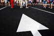 © Dmitry - Road marking arrow on the background of the feet of pedestrians. The direction indicator is painted with white paint on an asphalt road. Foreground. selective focus