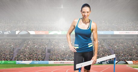 Wall Mural - Composite image of caucasian female athlete standing near a hurdle against sports stadium