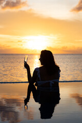 Wall Mural - Attractive woman on a infinity pool near the ocean with a glass of champagne.Back view