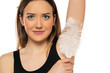 young smiling woman caressing the armpit with white feather on a white background