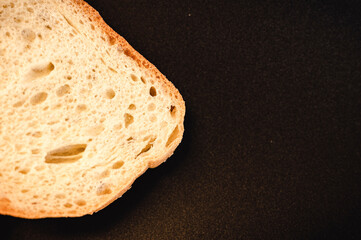 slice of white bread close up on a black background. rough dappled textured surface chopped piece loaf of natural organic food with holes. top view