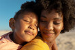© WavebreakMediaMicro - Close-up of african american girl with eyes closed relaxing on mother's shoulder at beach