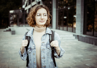 Wall Mural - Modern young student woman in stylish denim jacket and backpack outdoors