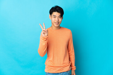 Poster - Young Chinese man isolated on blue background smiling and showing victory sign