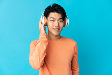 Poster - Young Chinese man isolated on blue background listening music