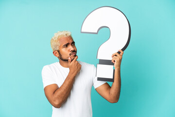 Wall Mural - Young Colombian handsome man isolated on blue background holding a question mark icon and having doubts