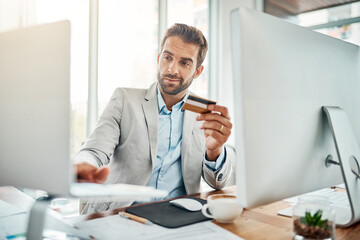 Poster - The ease of online banking. Shot of a handsome young businessman using a computer while holding a credit card in an office.