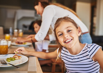 Canvas Print - Enjoying a delicious breakfast with her favourite people. Portrait of a little girl having breakfast with her family in the background.