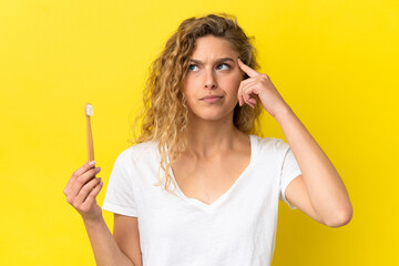 Wall Mural - Young caucasian woman holding a brushing teeth isolated on yellow background having doubts and thinking