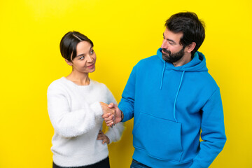 Wall Mural - Young caucasian couple isolated on yellow background handshaking after good deal