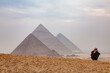 Egyptian man sitting on a hill with the blurred pyramids on the background, Cairo, Egypt.