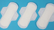 Woman sanitary napkins on blue background. Top view. Absorbent pads worn by women to absorb menstrual blood. Comfortable white sanitary napkins arranged on light blue paper. Represent Hygiene concept