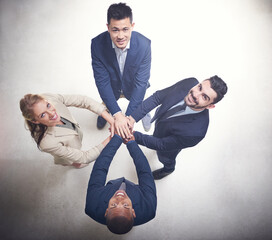 Poster - We know where our strength lies. High angle shot of a team of happy colleagues putting their hands on top of each other in the office.