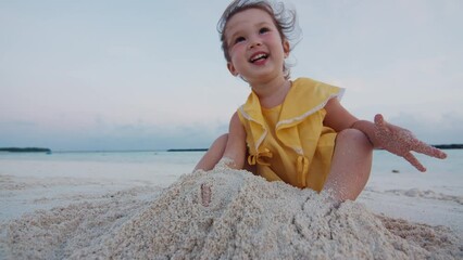 happy toddler girl plays with sand on the tropical beach in maldives