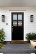 Black front door with windows that have a design element to them with two light fixtures and decorated with green plants