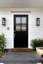 Black Front Door With Windows That Have A Design Element To Them With Two Light Fixtures And Decorated With Green Plants