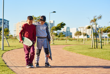 They share a common hobby. Shot of two young brothers walking together with their skateboards at the park.