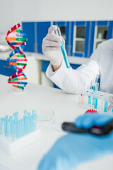 partial view of scientist holding test tube near dna model on blurred foreground.