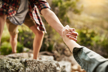 Alone we climb rocks, together we climb mountains. Cropped shot of hikers helping each other climb up a rock in nature.