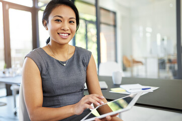 Accomplishing deadlines with ease thanks to technology. Portrait of a confident young businesswoman working on a digital tablet in a modern office.